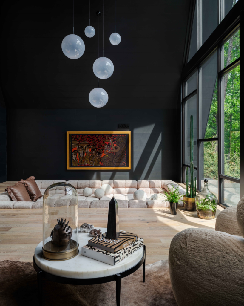 Living room conversation pit with pillows and a white bubble chandelier overhead. marble cocktail table and chairs in foreground and views to the green wooded exterior landscape