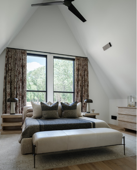 Primar bedroom with bed and nightstands floating in front of window and pitched ceiling and black ceiling fan; primary bath w/walk-in shower