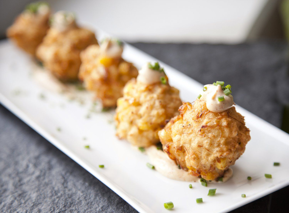 Maryland Blue Crab and Corn Fritters with Chipotle Aioli served on white platter with dollops of Chipotle Aioli and green onion garnish