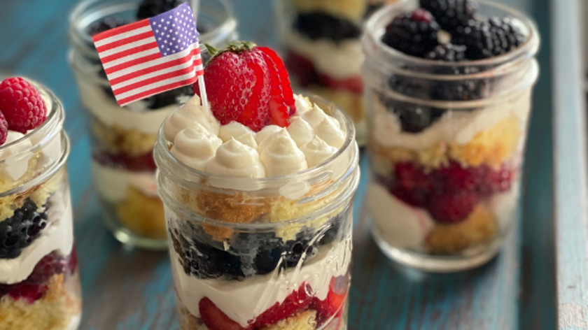 Fresh Berry Shortcake Cups serviced in mason jars in layers of red, white, and blue and a flag toothpick garnish