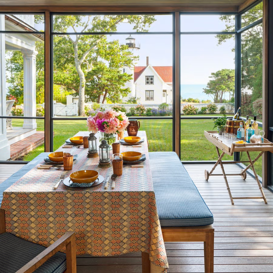 Festive summer tablescape on a screened porch with fresh flowers, Fiestaware, bar cart, cushioned bench and chair seating
