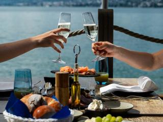 arms and hands toasting champagne glasses while on a dock setting with brunch fare overlooking the blue lake waters