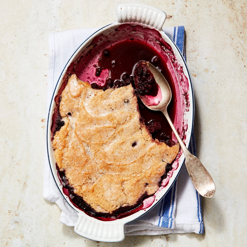 Blueberry Pancake Cobbler in an oval baking dish with a silver spoon full of blueberries