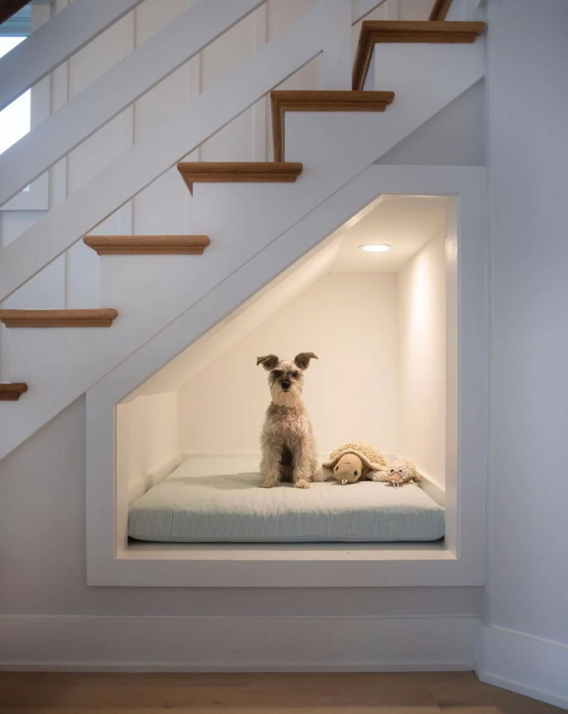 built-in dog bed underneath the stairs with a removable and washable pillow and recessed lighting; terrier mix sitting with his stuffed animals