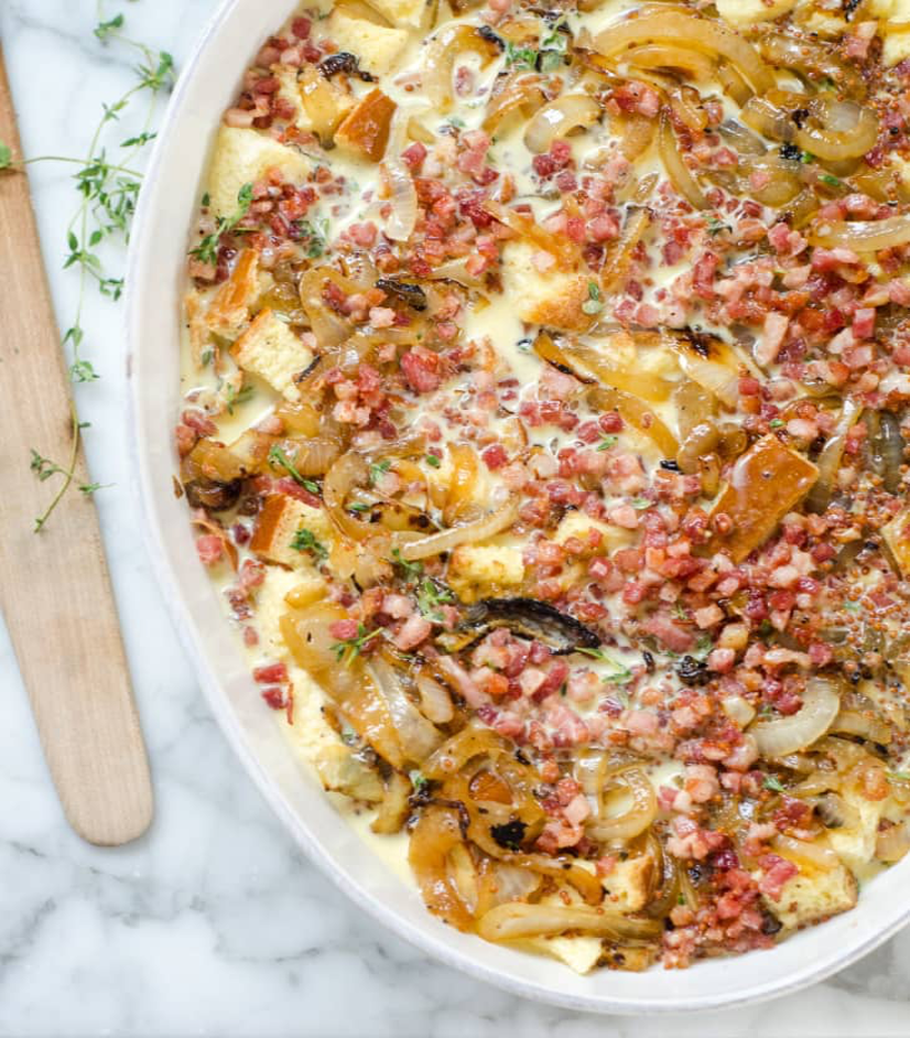 Make-Ahead Pancetta and Gruyère Breakfast Casserole served in a white casserole dish with green garnish and wooden utensil
