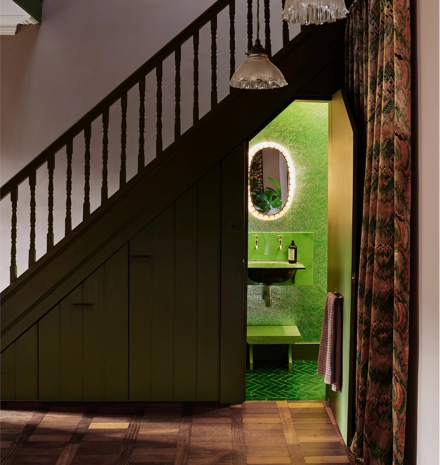 a hidden jewelbox powder room under the stairs in vibrant shades of green and luxe bathroom elements
