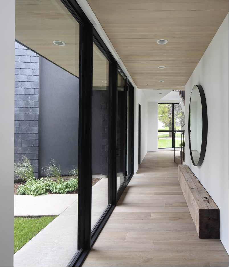 Clad in white oak and minimalist accents, the narrow hallway in the central vestibule offers a graceful prelude to the serene spaces that await inside.
