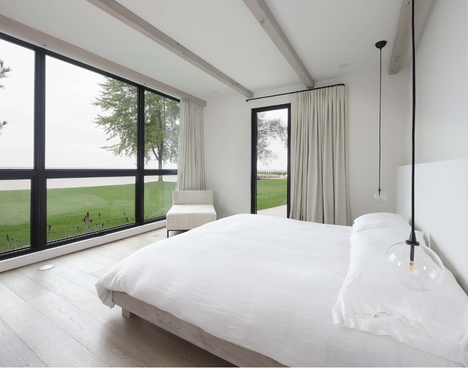 Dressed in white with minimal decorative accents, the primary bedroom offers the homeowners a tranquil escape from which to enjoy the expansive lake views outside.