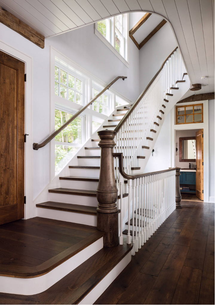 Well-Worn Patinas and rustic woods incorporated into the entrance staircase of lake home with wide-plank stained floors and wood detailing