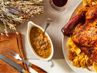 Caramelized Onion Gravy in a gravy boat on a Thanksgiving table with turkey, utensils, table linens, and wine in the background.
