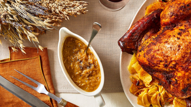 Caramelized Onion Gravy in a gravy boat on a Thanksgiving table with turkey, utensils, table linens, and wine in the background.