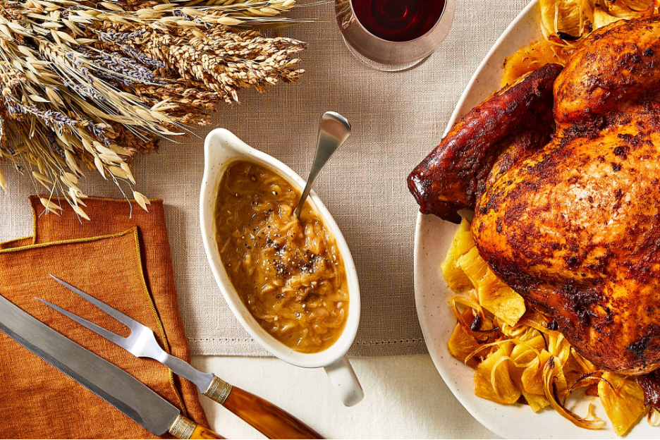 Caramelized Onion Gravy in a gravy boat on a Thanksgiving table with turkey, utensils, table linens, and wine in the background.
