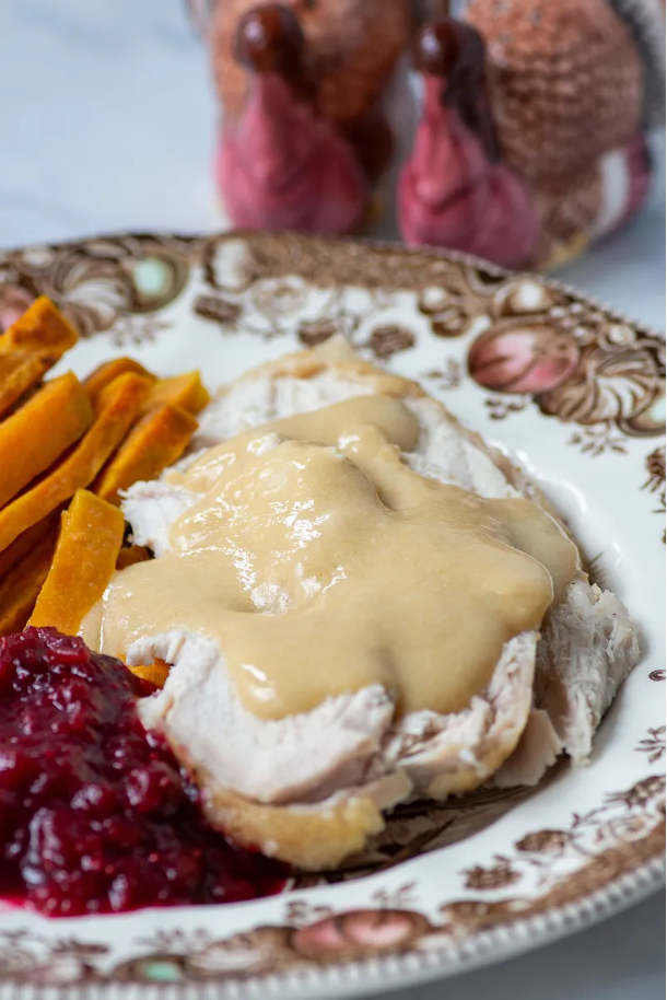 Easy Gluten-Free Turkey Gravy on top of turkey with sweet potatoes and cranberry sauce on the side and turkey decorations in backdrop