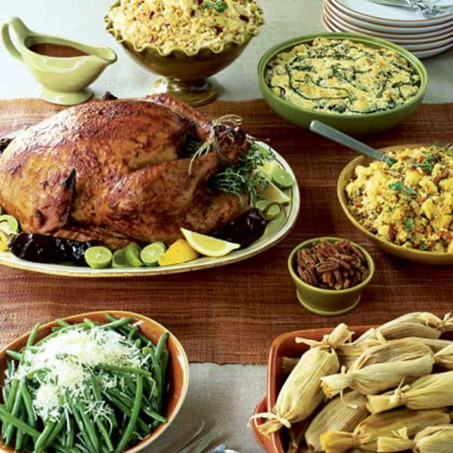 Roasted Poblano Gravy in a green gravy boat beside a Guajillo-Tamarind turkey and all the side dishes on a table