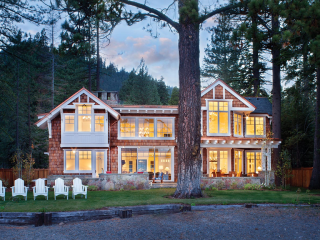 Classic Adirondack-style lake home with shingled cladding, white gables and trim, and a line of white Adirondack chairs lining the shore.