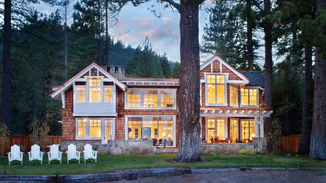 Classic Adirondack-style lake home with shingled cladding, white gables and trim, and a line of white Adirondack chairs lining the shore.