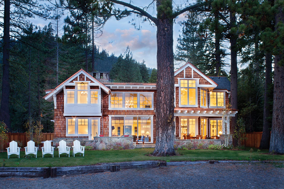 Classic Adirondack-style lake home with shingled cladding, white gables and trim, and a line of white Adirondack chairs lining the shore.