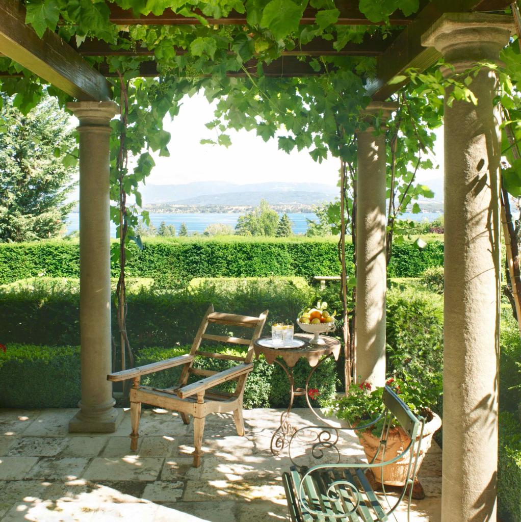 Small garden niche with pergola overhead draped in greenery, overlooking a lake setting