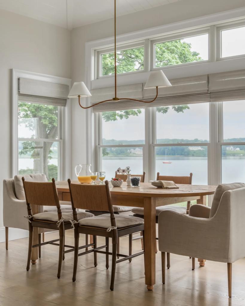 A waterfront home's dining room with a Lightened, Water-Inspired Color Palette that displays picturesque water views in summer
