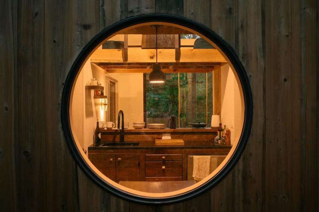 Japandi-style kitchen in a tiny home in the woods with porthole window surrounded by shou sugi ban exterior