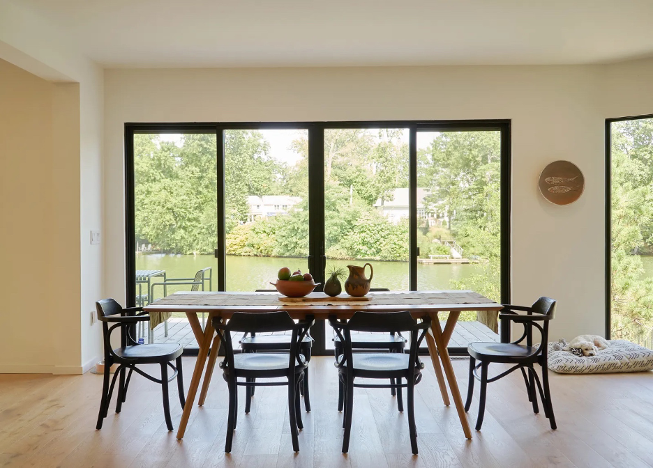 Japandi-style dining area in front of a wide glass expanse overlooking a lake