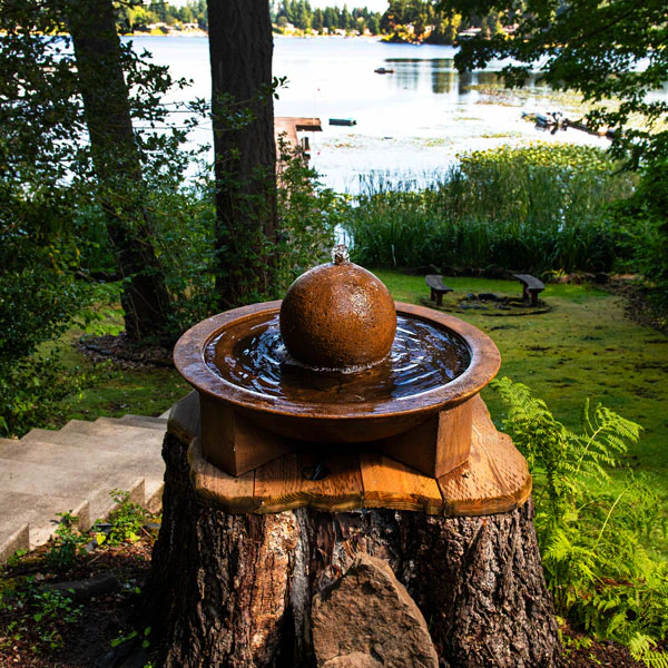 Zen fountain on top of old tree stump in a lake setting.